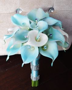 a bridal bouquet with blue and white flowers on a wooden table next to a couch