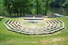 an outdoor seating area in the middle of a grassy field next to a body of water