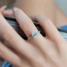 a woman's hand holding a cell phone with an engagement ring on top of it