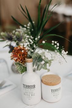 there are two bottles on the table next to each other with flowers and greenery in them