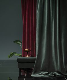 a black piano sitting in front of a red curtain next to a potted plant