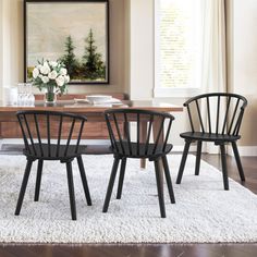 three black chairs sitting on top of a white rug in front of a wooden table