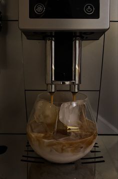 coffee being poured into a glass bowl in front of a microwave on a tiled wall