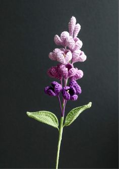 a crocheted purple flower is shown in front of a black background with green leaves