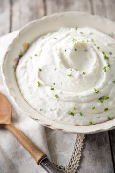 a white bowl filled with mashed potatoes sitting on top of a table next to a wooden spoon