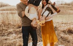 a man and woman holding two babys in their arms while standing on a blanket