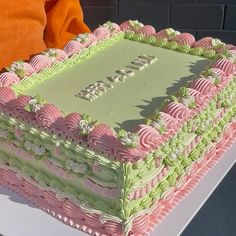 there is a large cake with pink and green frosting on the table next to orange pillows