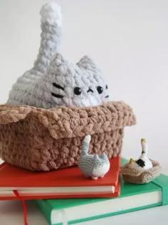 a crocheted basket sitting on top of a pile of books next to a small toy cat