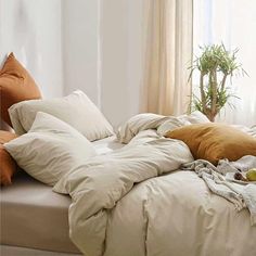 an unmade bed with several pillows and blankets on it in a bedroom area next to a potted plant