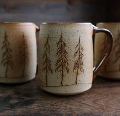 three coffee mugs sitting on top of a wooden table next to eachother