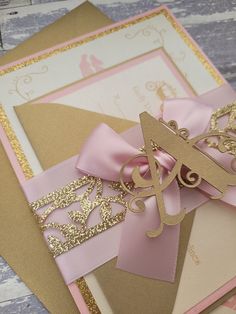 a pink and gold wedding card with a monogrammed letter on it's side