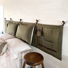 a bed with four pillows hanging on the wall next to a stool and pillow case