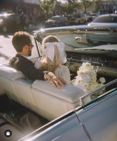 a bride and groom sitting in the back of a convertible car on their wedding day