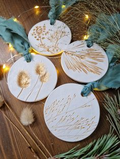 four handmade coasters decorated with dried plants and lights on a wooden table surrounded by greenery