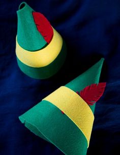 two green and yellow hats with red feathers on them sitting on a blue surface together