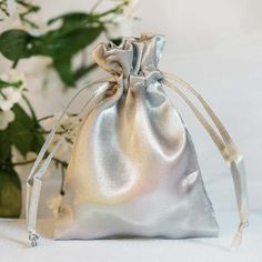 a silver satin bag sitting on top of a white table next to a vase filled with flowers