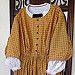 a yellow dress with white collar and sleeves on display in front of a wooden door