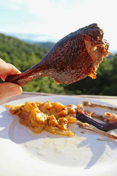 a person is holding a piece of meat over some food on a white plate with mountains in the background