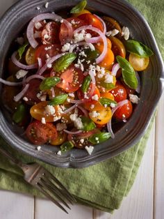 a bowl filled with tomatoes and onions on top of a green napkin next to a fork