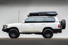 a white suv with luggage strapped to it's roof rack in front of a wall