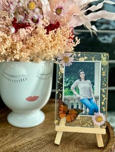 a vase filled with flowers next to a photo on a wooden stand and a butterfly