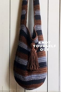 a crocheted bag hanging on a wall with a hook in the middle that has a tasseled handle