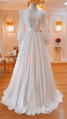 a white wedding dress on display in a room with wooden floors and chandeliers