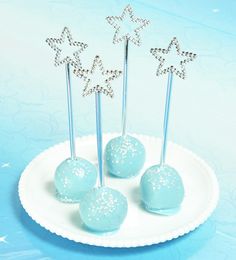 four blue cake pops on a white plate with silver star toppers and sparklers