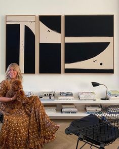 a woman sitting on a chair in front of two paintings and a table with chairs