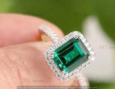 an emerald and diamond ring on someone's finger