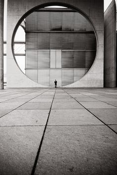 a black and white photo of a person standing in front of a large circular building