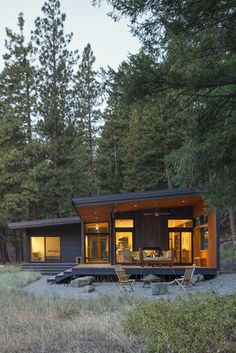 a small cabin in the middle of a forest at night with its lights on and windows open