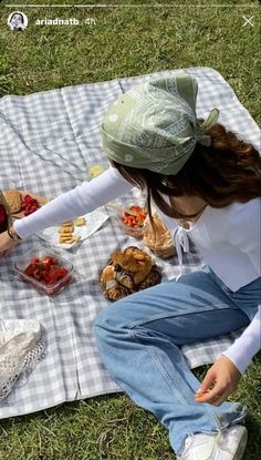 a woman sitting on top of a blanket next to a picnic table filled with food