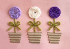 three flower pots with different colored yarn flowers in them on a pink tablecloth