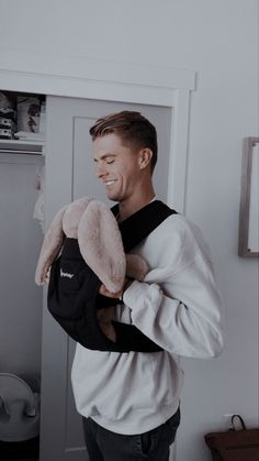 a man is holding a stuffed animal in his arms and smiling at the camera while standing next to a door