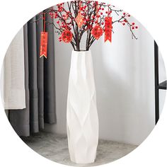 a white vase with red flowers in it on a table next to curtains and clothes