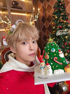 a young man holding up a christmas tree with snowmen on it in front of a decorated christmas tree