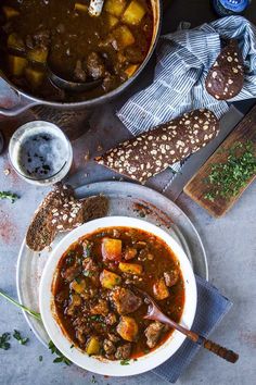 a bowl of stew next to bread on a table