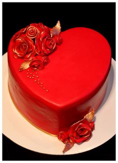 a red heart shaped cake with roses on it's side and gold trimmings