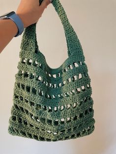 a hand holding a green crocheted bag with holes on the front and sides