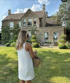 a woman standing in front of a large house with a wicker basket on her shoulder