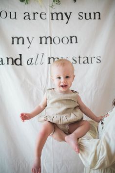 a baby sitting on the back of a chair in front of a sign that says you are my sun, my moon and all my stars