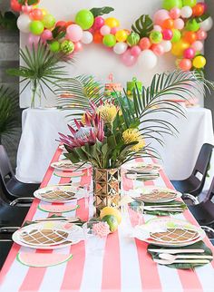 the table is set with plates, silverware, and fruit for a tropical themed party