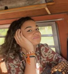 a woman sitting in the back of a vehicle with her hand on her head and looking off into the distance