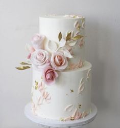 a three layer white cake with pink and gold flowers on the top, sitting on a stand