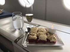 an airplane tray with dessert and wine on it next to a glass of water in the foreground