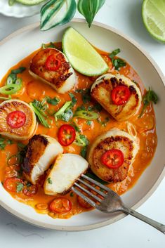 a white plate topped with scallops covered in sauce and garnished with tomatoes