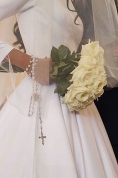 a woman in a white wedding dress holding a flower and a cross on her arm