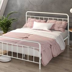 a white bed with pink sheets and pillows in a room next to a potted plant