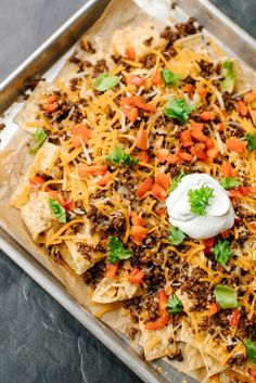 a tray filled with nachos topped with cheese and sour cream on the top